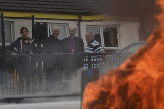 Bishops Good and McKeown look on as van burns during rioting.  Image: Church of Ireland