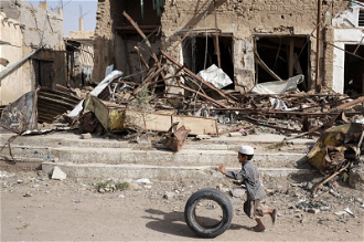 Boy runs with his tyre past buildings damaged by air strikes in Saada Old Town - Image: Giles Clarke / OCHA