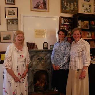 A tour leader with two Sisters, in front of a depiction of the famous fireside scene