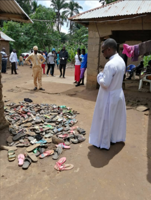 Fr Sam Ebute  in front of shoes of the dead  ©Aid to the Church in Need