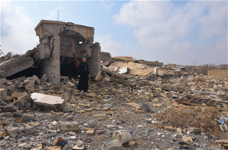 Priest standing amid ruins of building in Bashiqa destroyed during IS occupation  image ©ACN