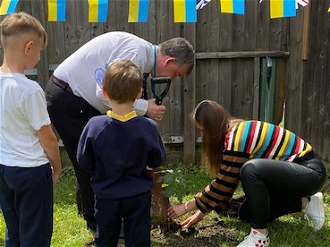 John Lane planting tree with the assistance of Ukrainian mother, as two pupils look on. Photo: Christ the King Catholic Primary School