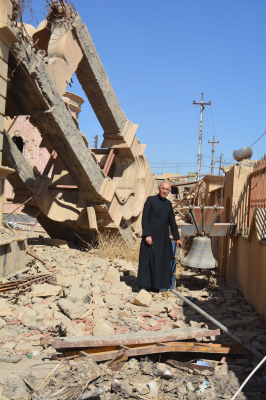 Fr George Jahola next to church's ruined bell tower in 2017 © ACN.
