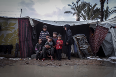 Family outside mud soaked tent Image NRC