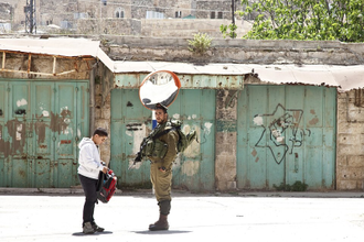 Israeli solider searches boy's school bag in Hebron. The boy is a member of one of the few remaining Palestinian families to live in the old centre of Hebron. Palestinians who do not live there are not allowed enter. Photo: Alan Whelan.